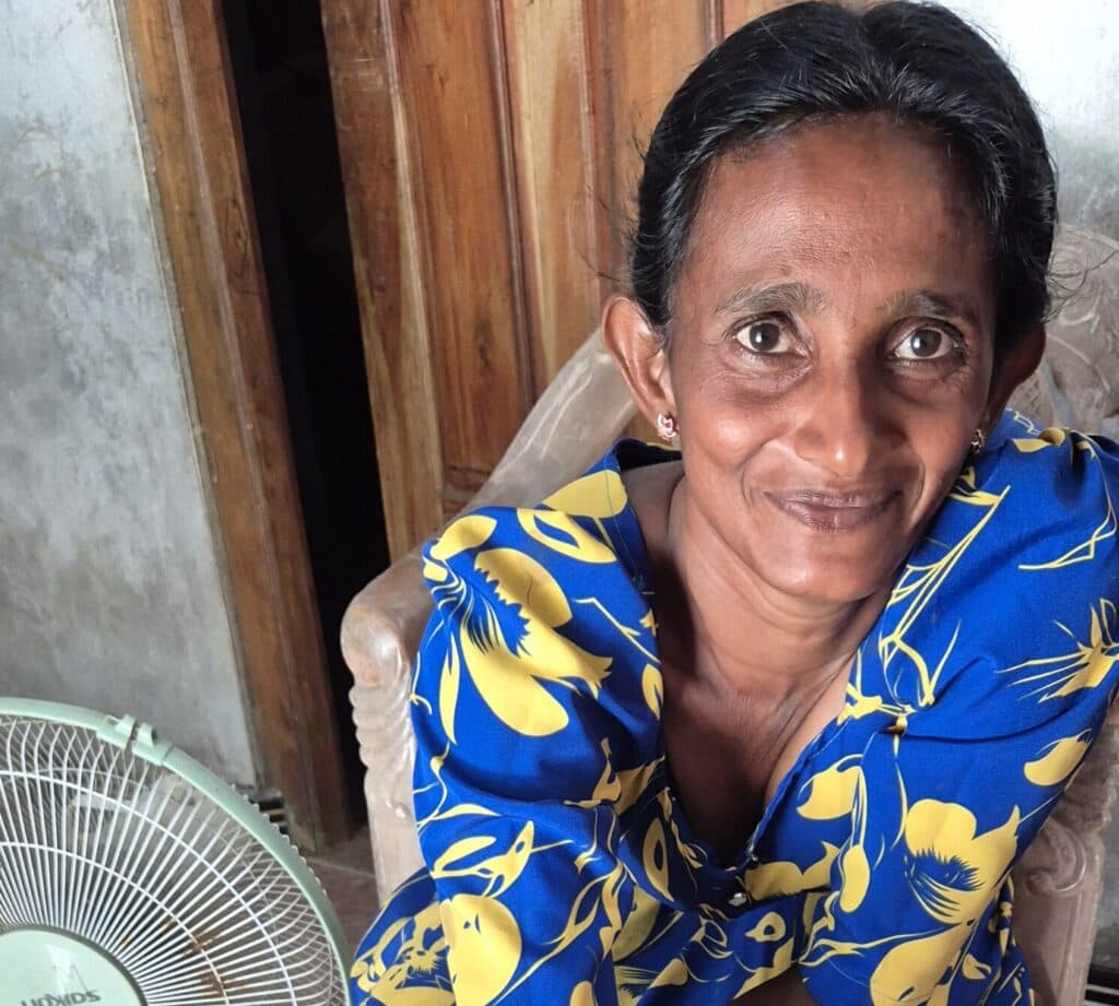A portrait of South Asian woman in a blue and yellow dress showing seeds in her right hand