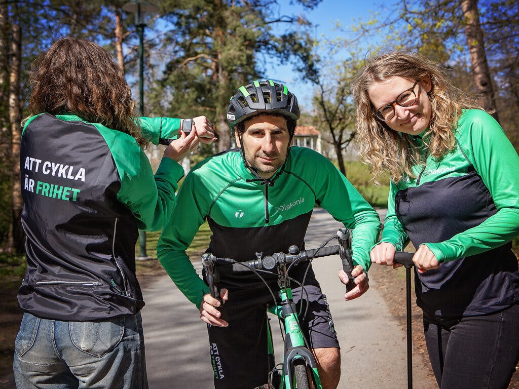 Tre personer i gröna cykelkläder och en cykel i mitten.