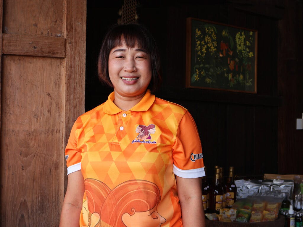 A woman with brown hair in an orange t-shirt is looking in to the camera and smiling.