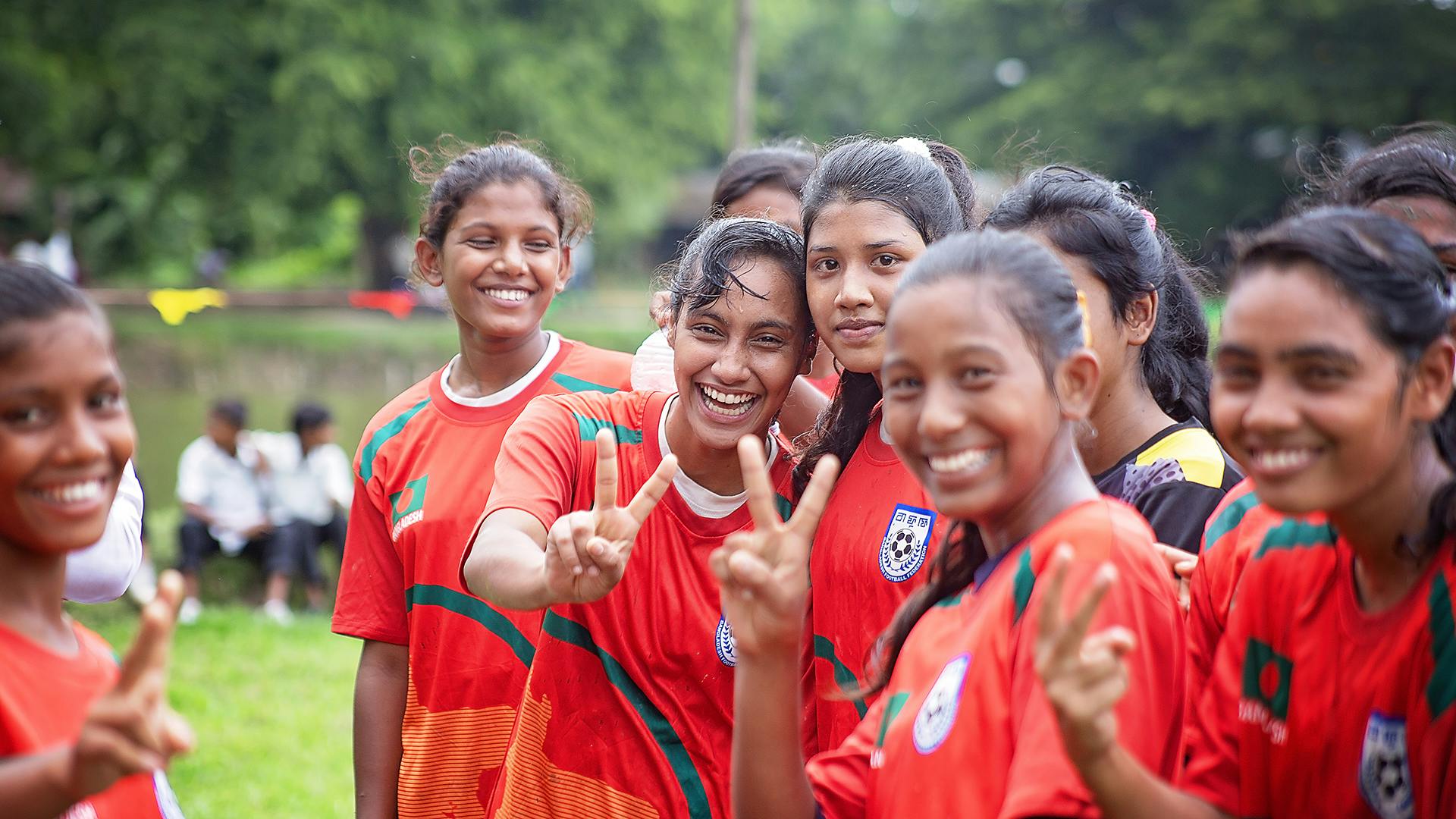 A group of girls in red football t-shirts cheering and smiling to the camera.