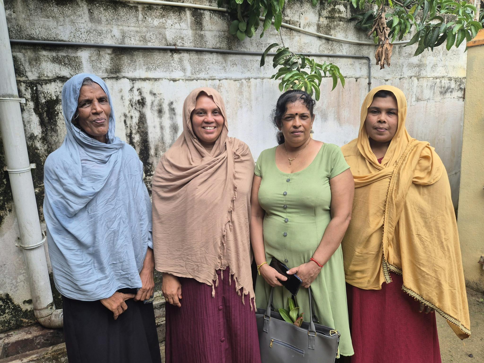 Four women standing in front of a wall with a tree, looking in to the camera