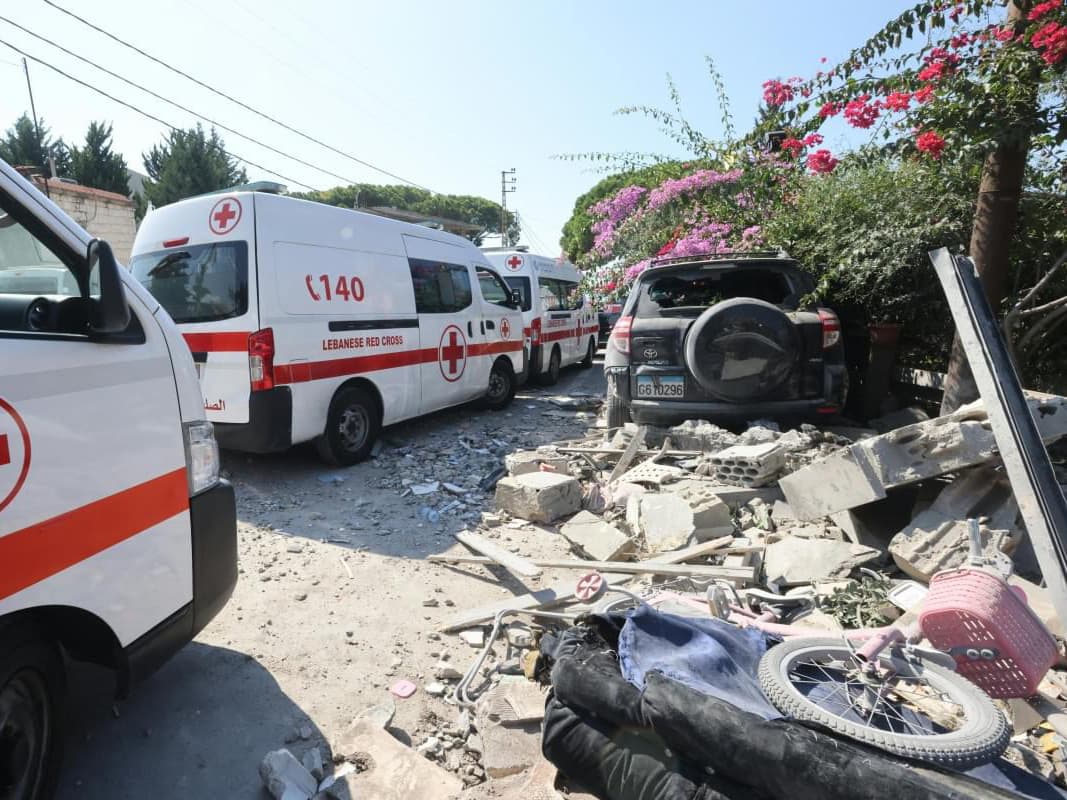 An ambulance marked "Red Cross Lebanon" and a destroyed building.