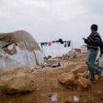 A boy walking through a camp with tents.