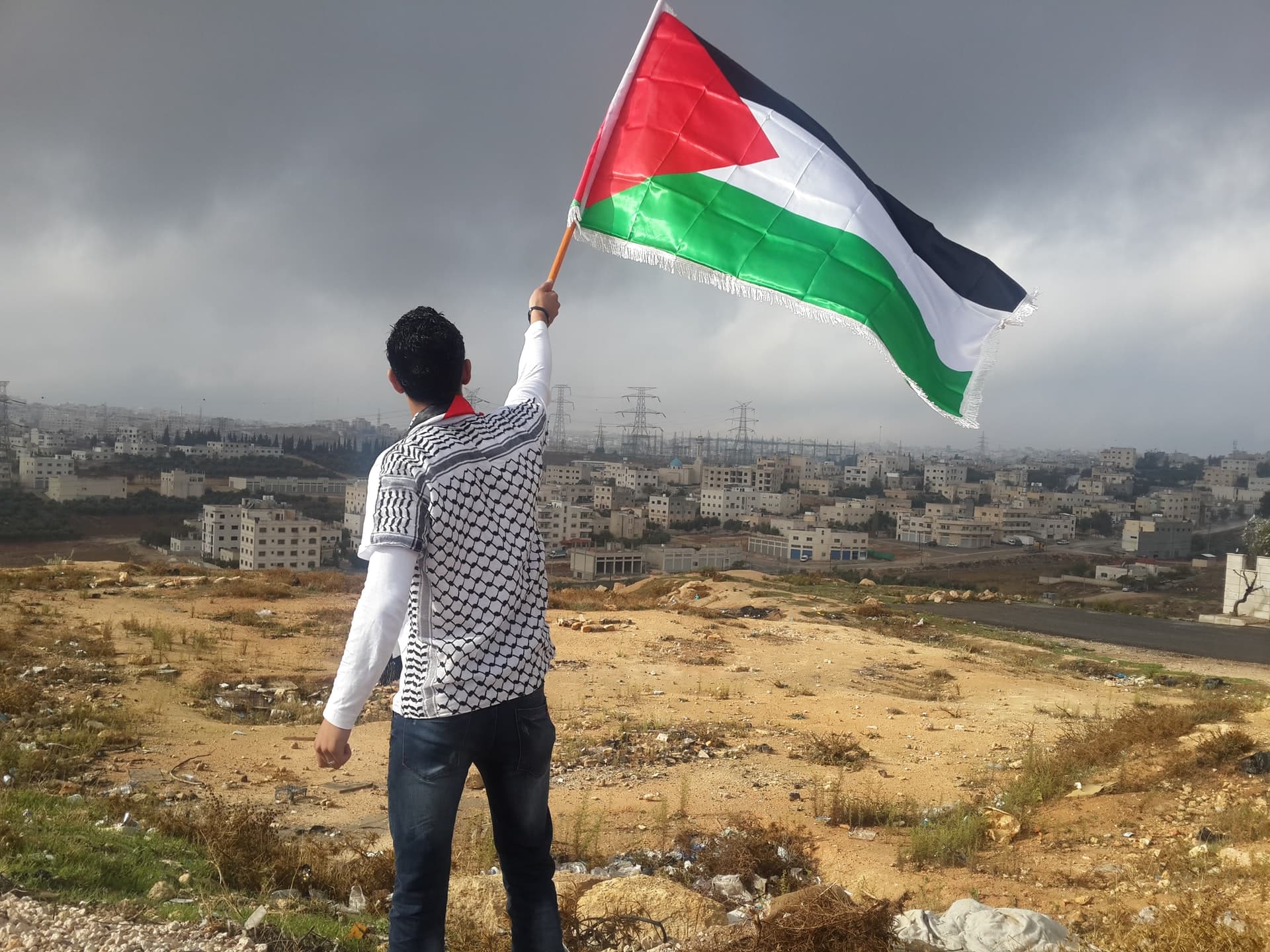 A young man waving a Palestinian flag. In the background Palestinian houses. A young man waving a Palestinian flag. In the background Palestinian houses.