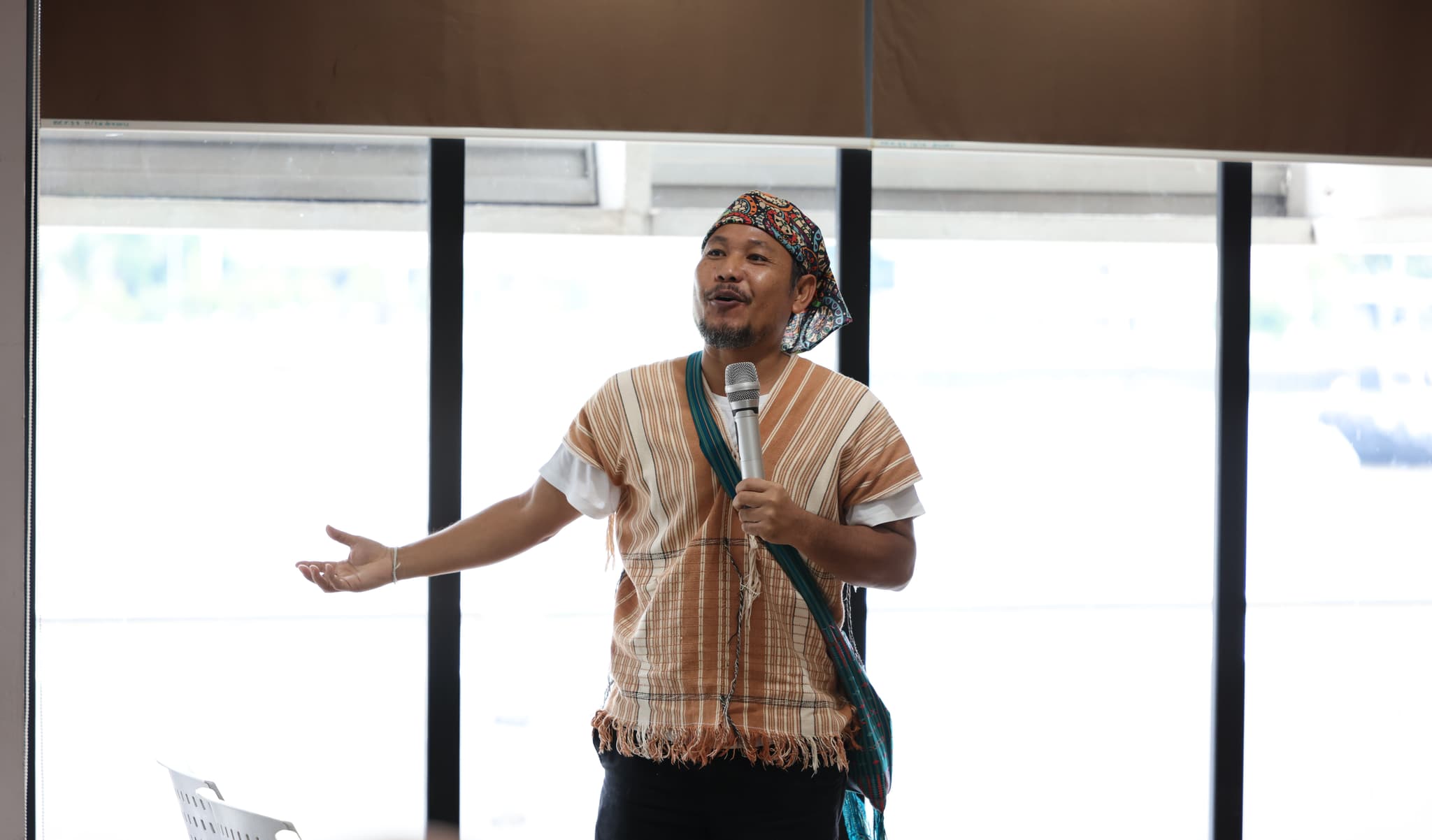 Kriangkrai, a man in traditional attire speaking into a microphone in front of a group