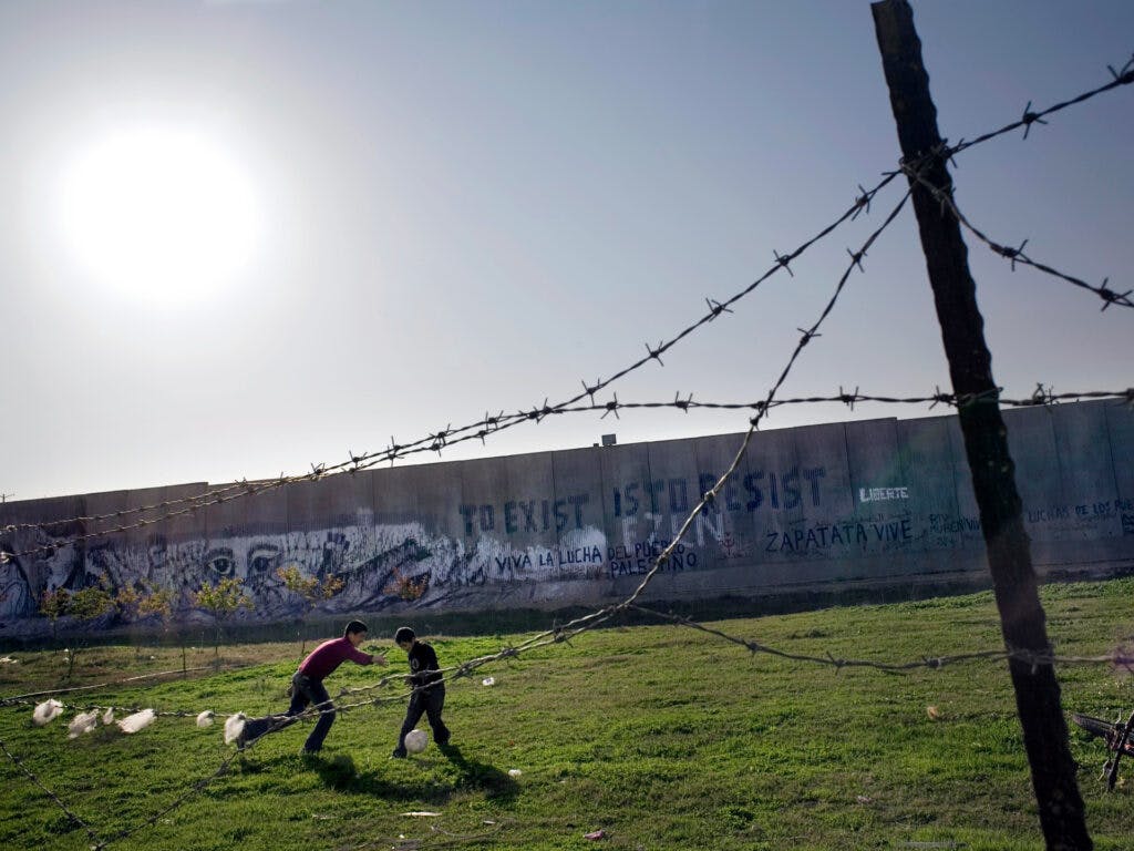 Två barn spelar fotboll framför muren i Palestina