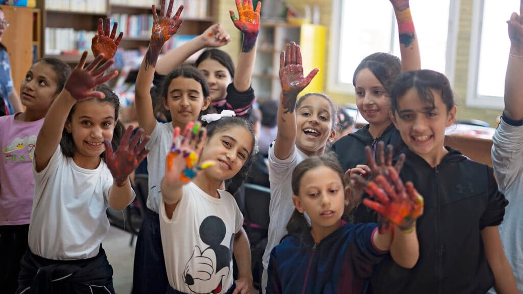 En grupp barn med målade händer i ett klassrum ler mot kameran.