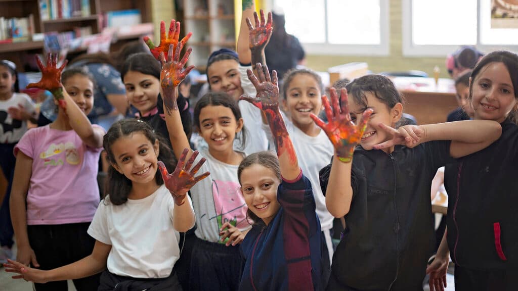 Foto: Ahmad Daghlas Flera barn i en grupp med målarfärg på händerna ser in i kameran och ler.