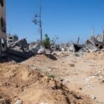 A person cleaning up rubble, with destroyed buildings in the background.