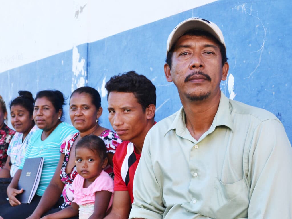 Photo: Diakonia Portrait of a man looking into the camera, in the background there is a group of people.