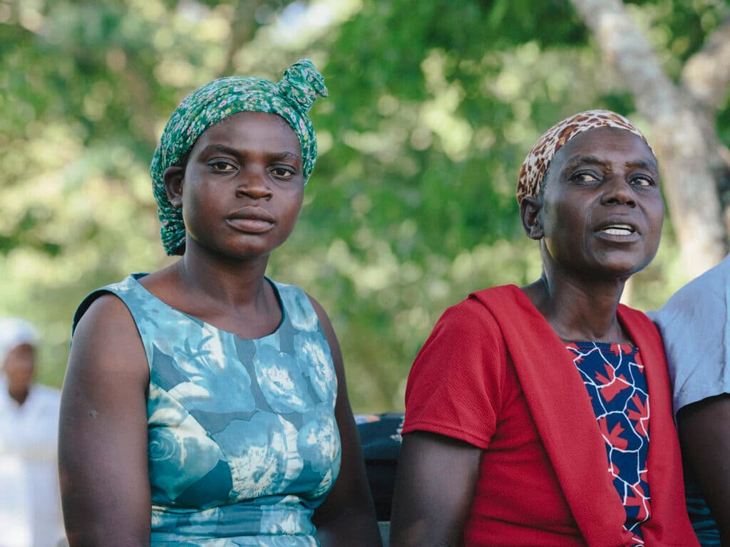 Two Zimbabwean women sitting next to each other. Behind them there are trees.