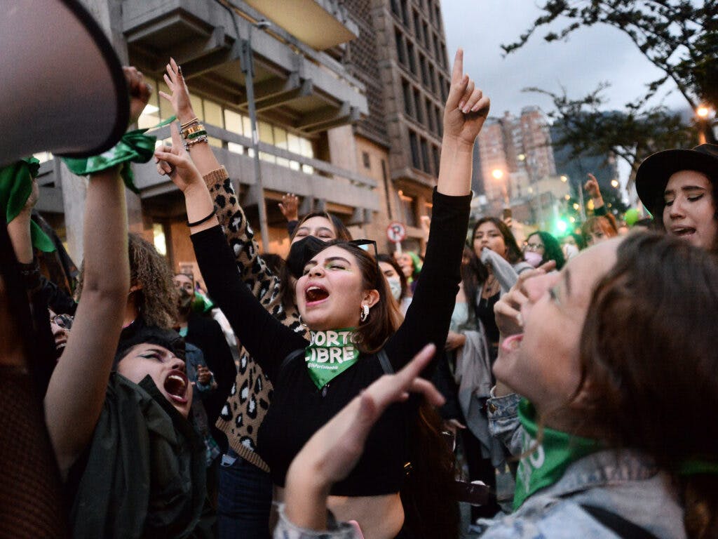 A crowd of young women lifting their hands and screaming, wearing green scarves.