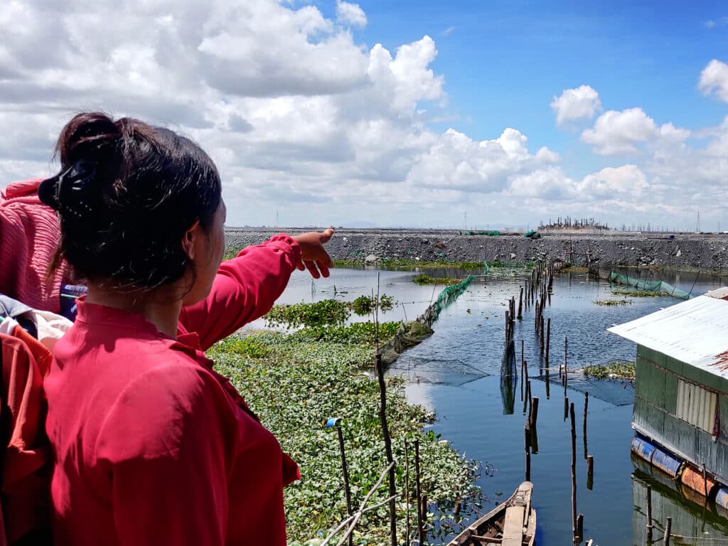 A woman with her back against the camera is pointing her hand towards a water area.